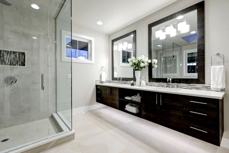A bathroom with two sinks , two mirrors and a walk in shower.
