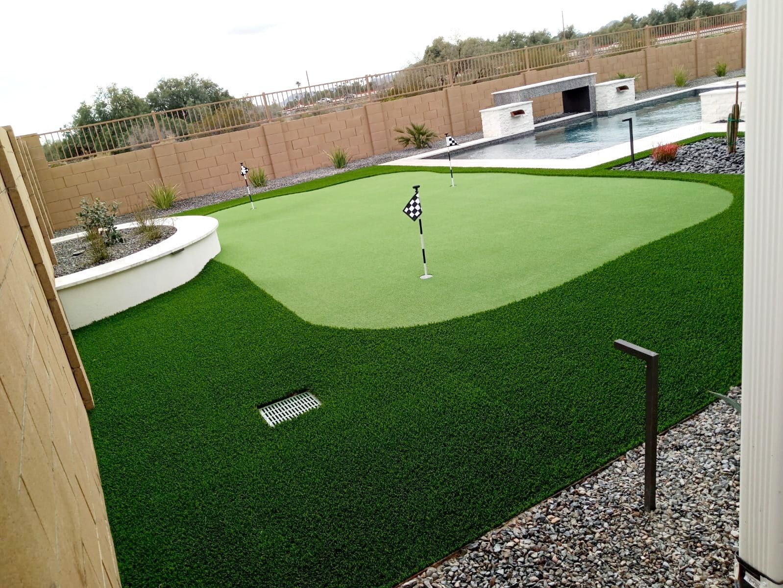 A putting green in a backyard next to a pool.