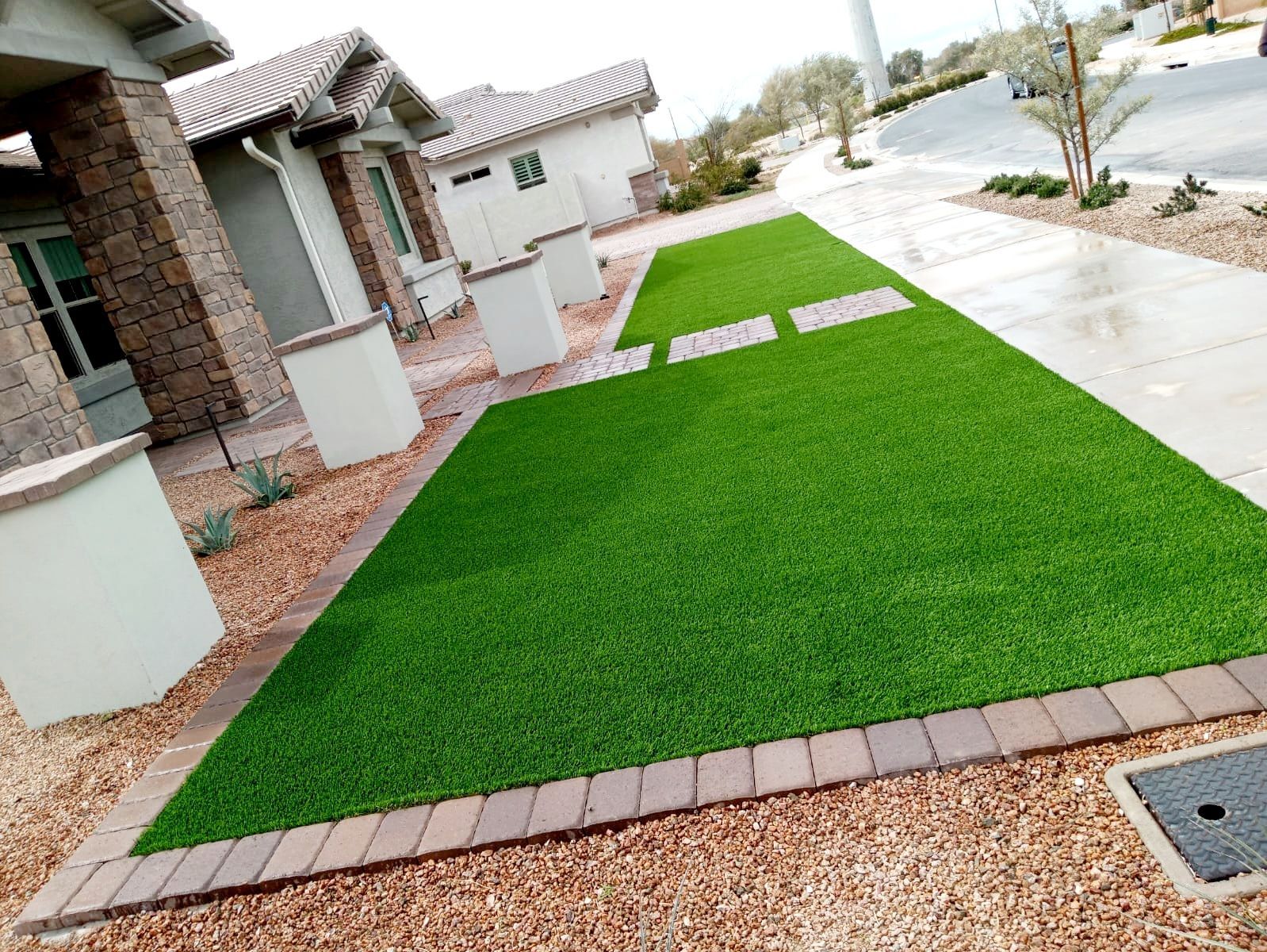 A lawn with artificial grass and bricks in front of a house.