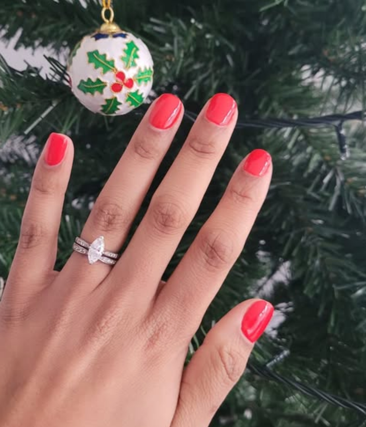 Hand with red nails displaying a ring, next to a Christmas ornament and tree.