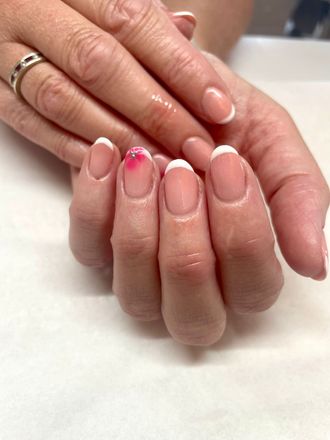 Hands with French tip manicured nails; one nail has pink and red accents.