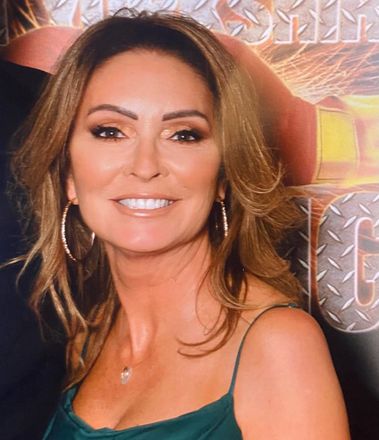 Woman with brown hair smiles, wearing hoop earrings and a green dress.