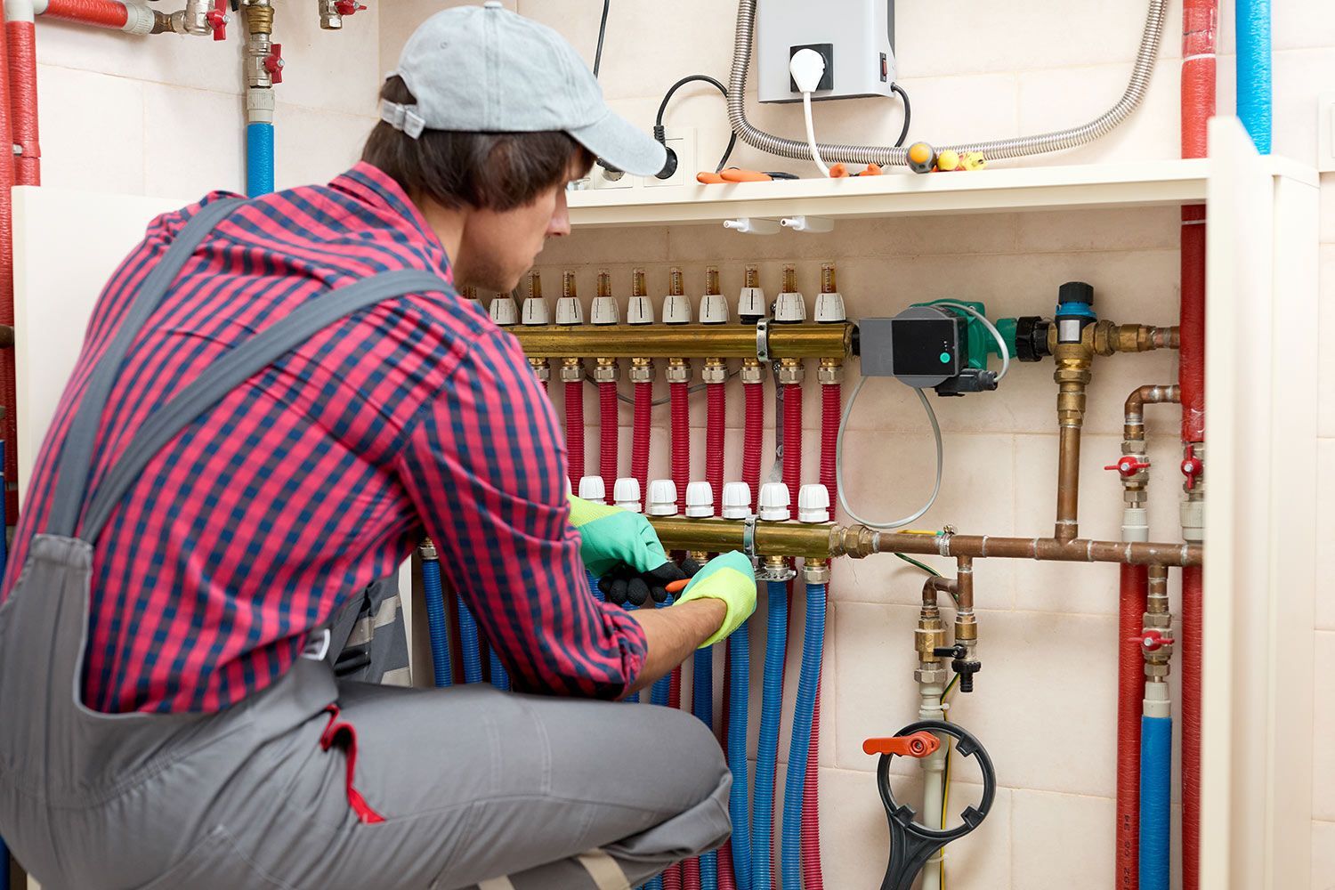 A technician adjusting a plumbing manifold with red and blue PEX pipes.