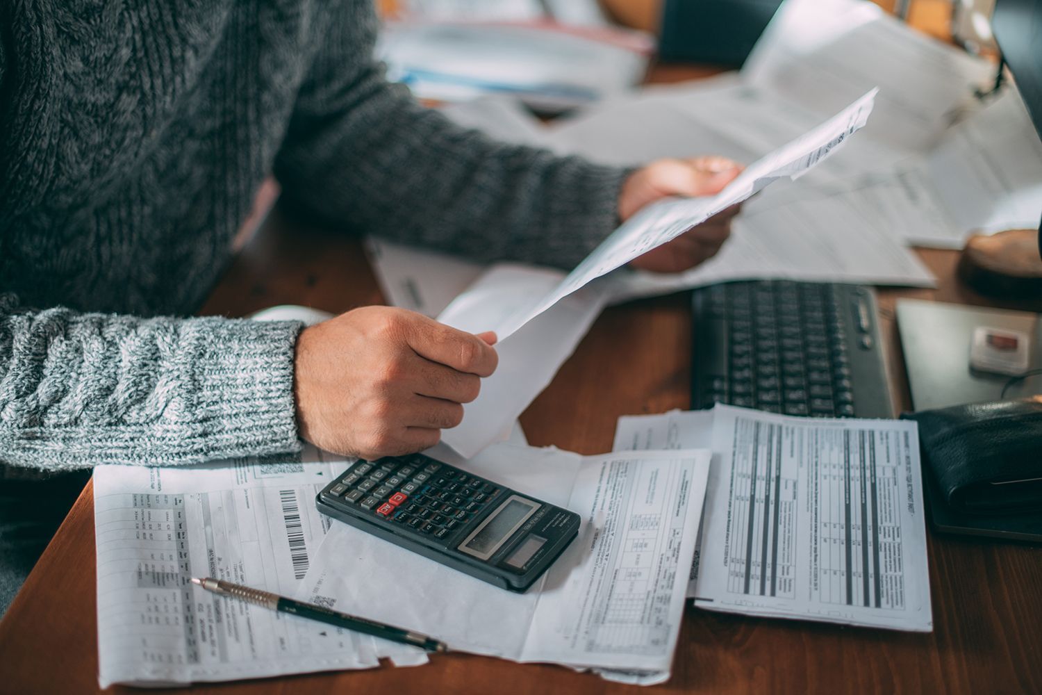 Person reviewing heating bills at a desk with papers, a calculator, and a keyboard.