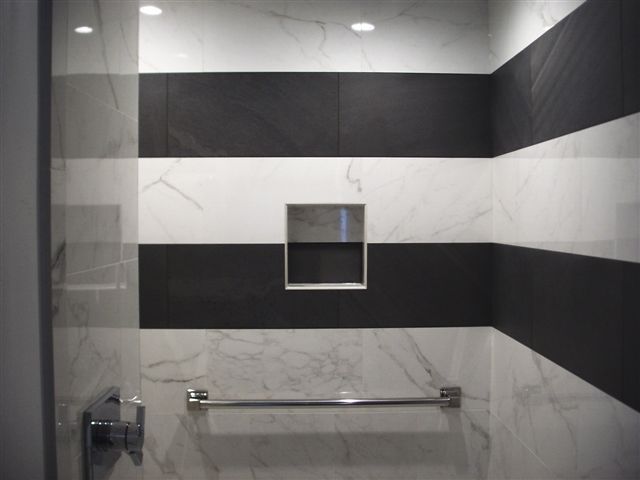 Shower with black and white striped tile. Recessed shelf and towel bar installed.