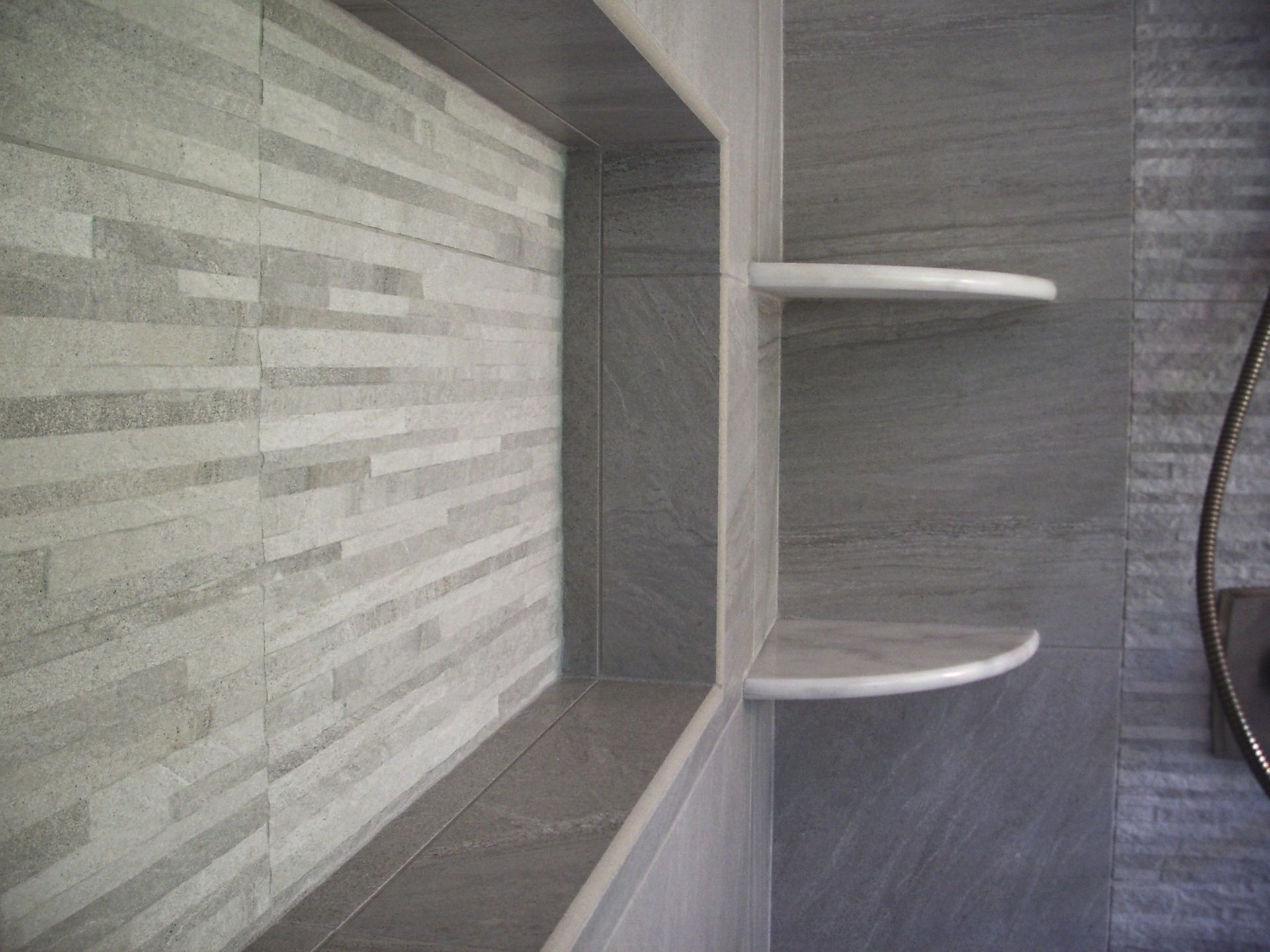 Gray tiled shower with a built-in rectangular niche and two rounded shelves.