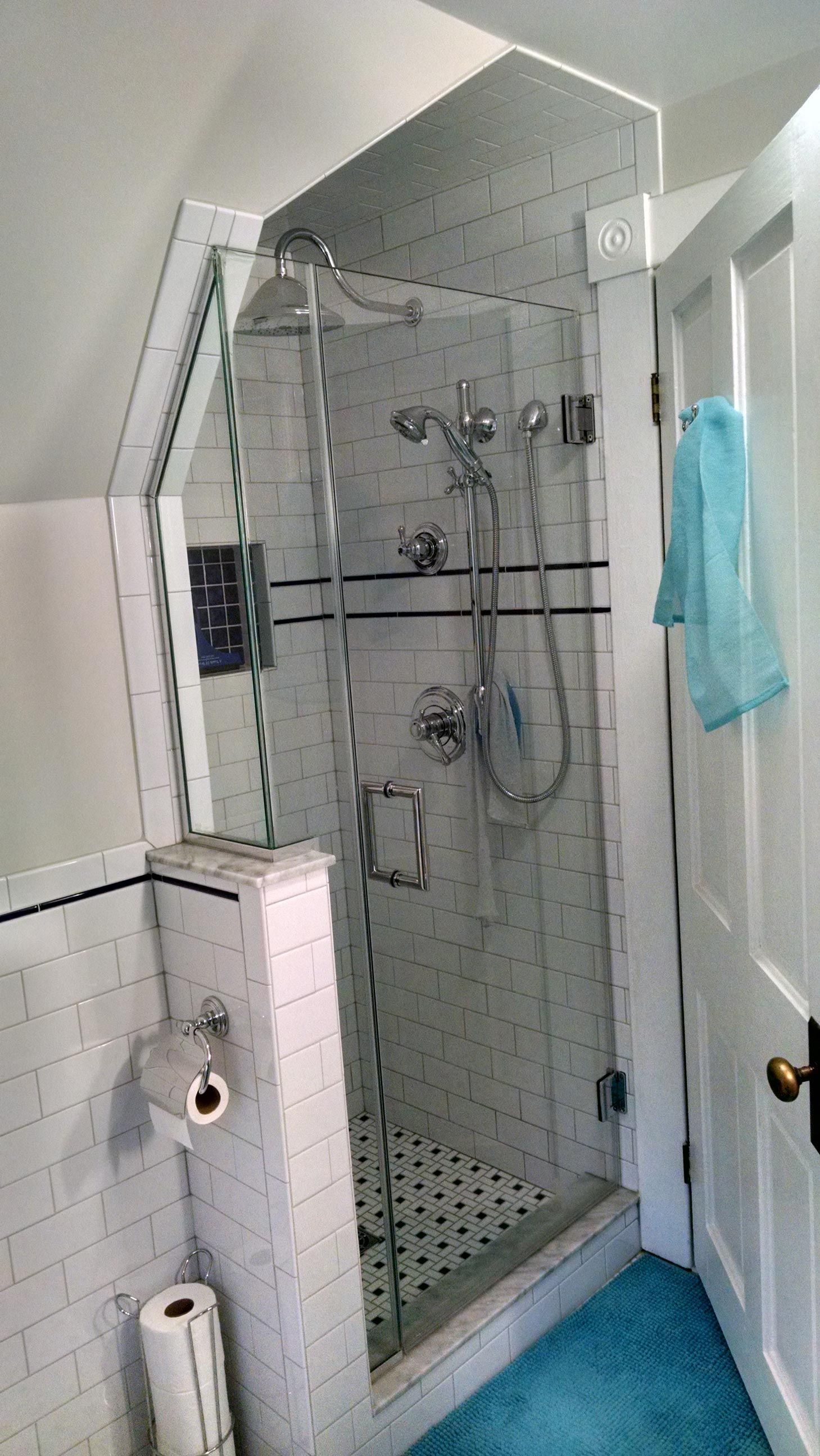 Shower with glass doors and white tiled walls. Blue towel hangs on white door.