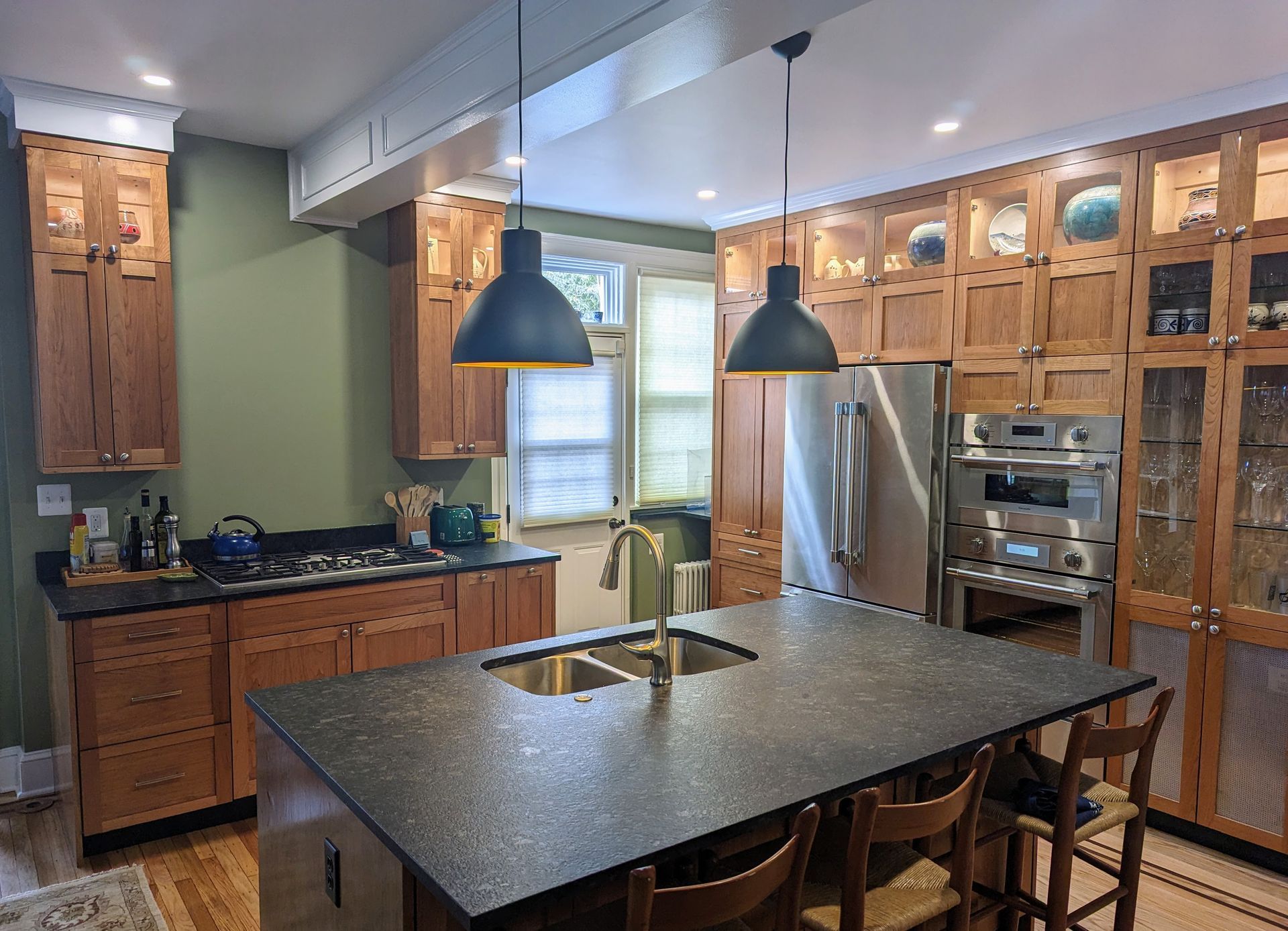 Kitchen with dark island, wood cabinets, stainless steel appliances, and black pendant lights.