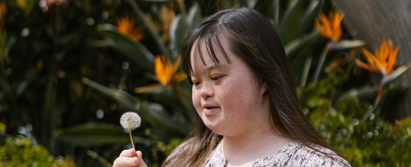 Woman holding a dandelion in a garden.