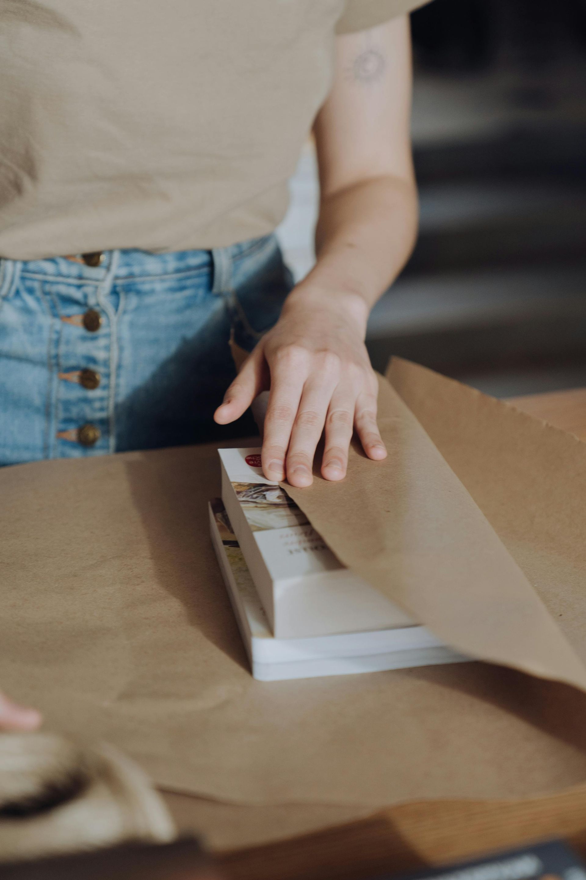 Person wrapping books in brown paper at a table.