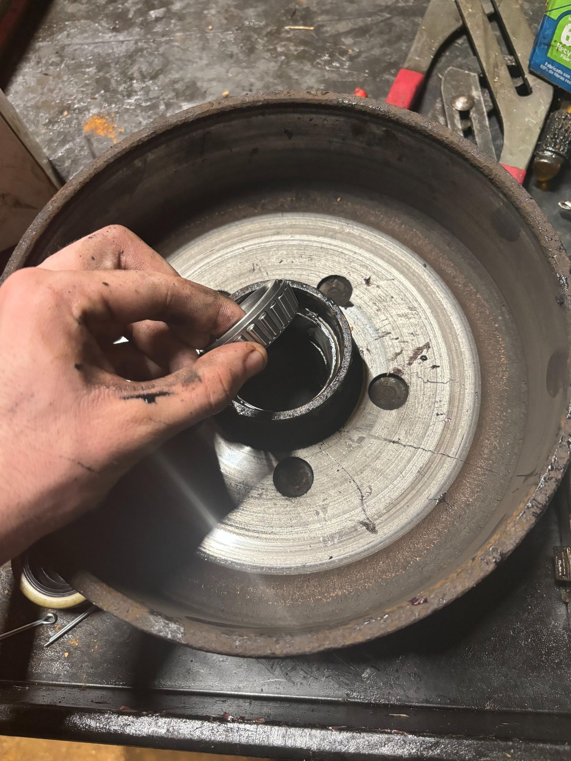 A person's hand holding a wheel bearing over the center hub of a brake drum.