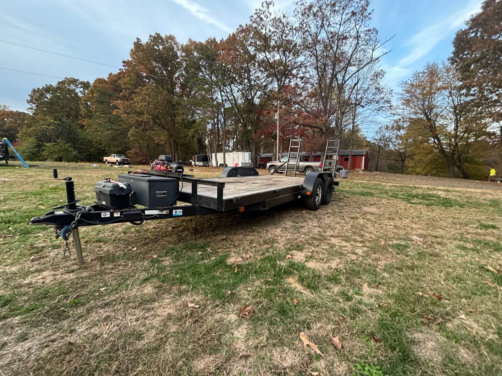 Flatbed trailer on brown grass in a yard, with trees in the background.
