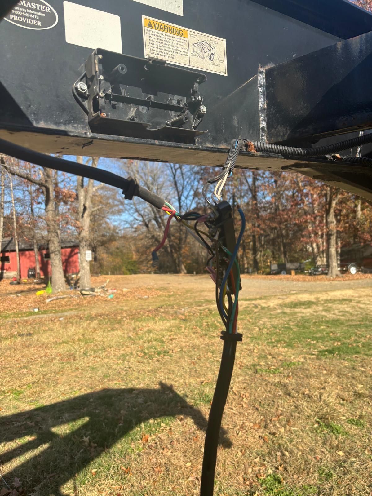Black trailer hitch with exposed wires and a field background.