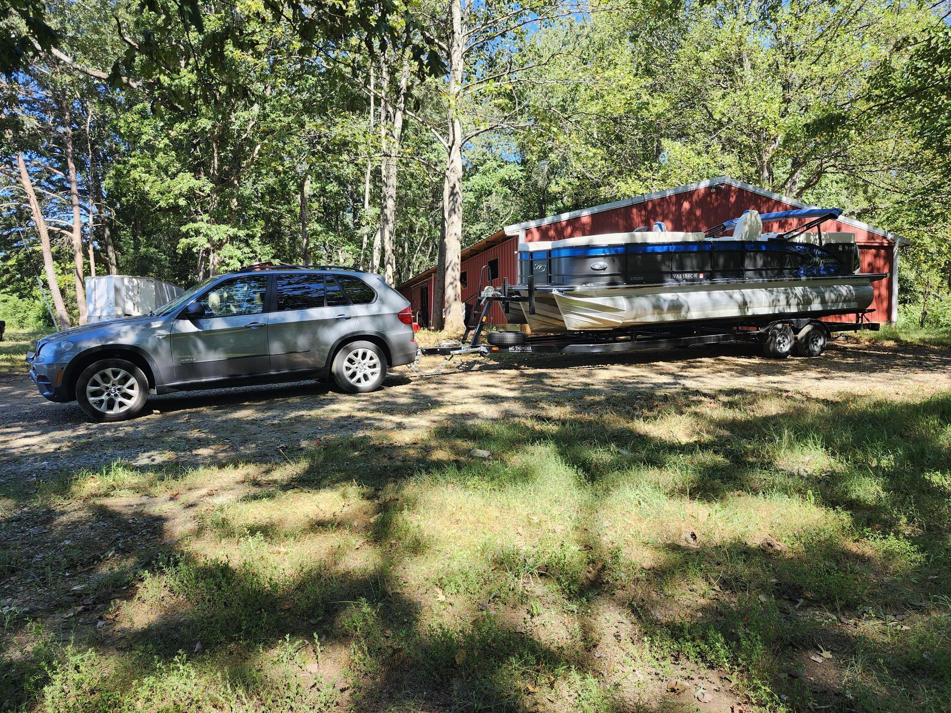 Gray SUV next to a boat on a trailer, parked near a red shed, trees in the background.