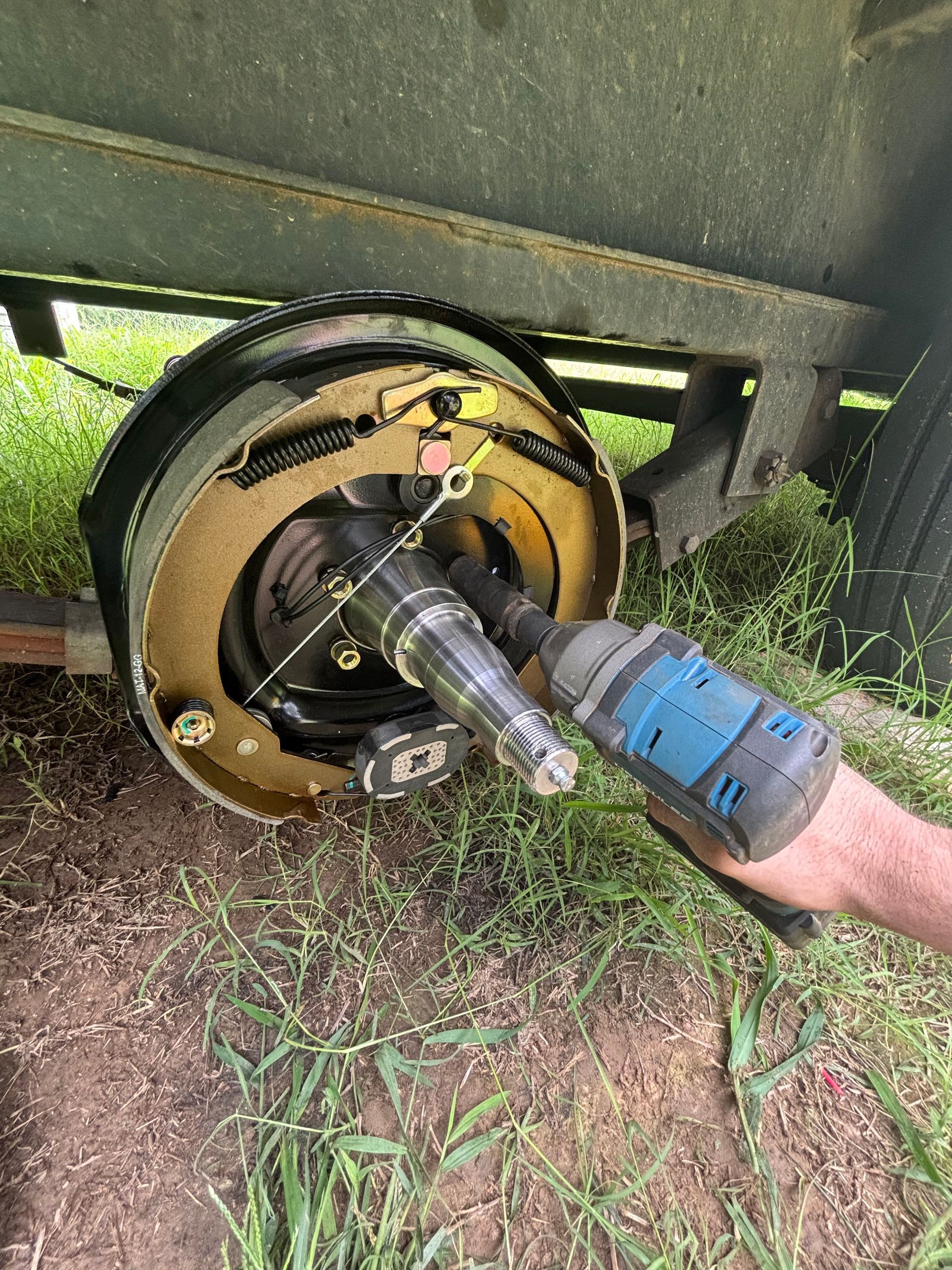 A person removes a trailer wheel hub, using a power tool outdoors.