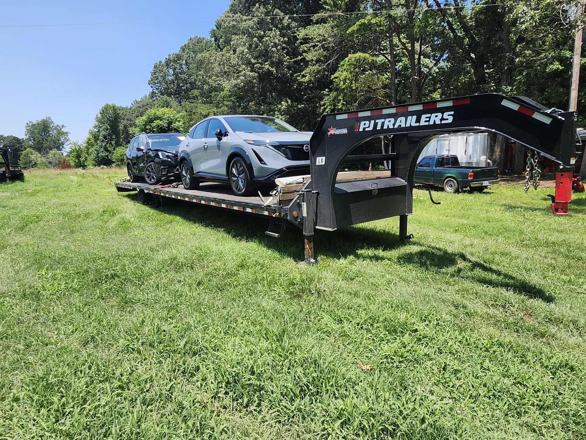 Silver car and motorcycle on a flatbed trailer in a grassy area on a sunny day.