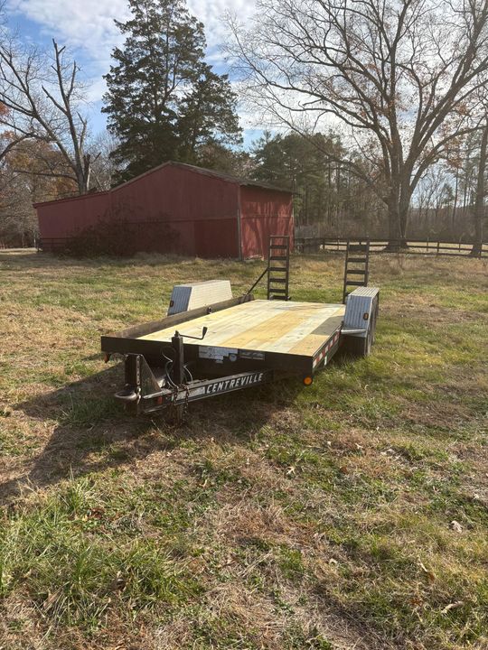 Black utility trailer on grass, red barn in background.