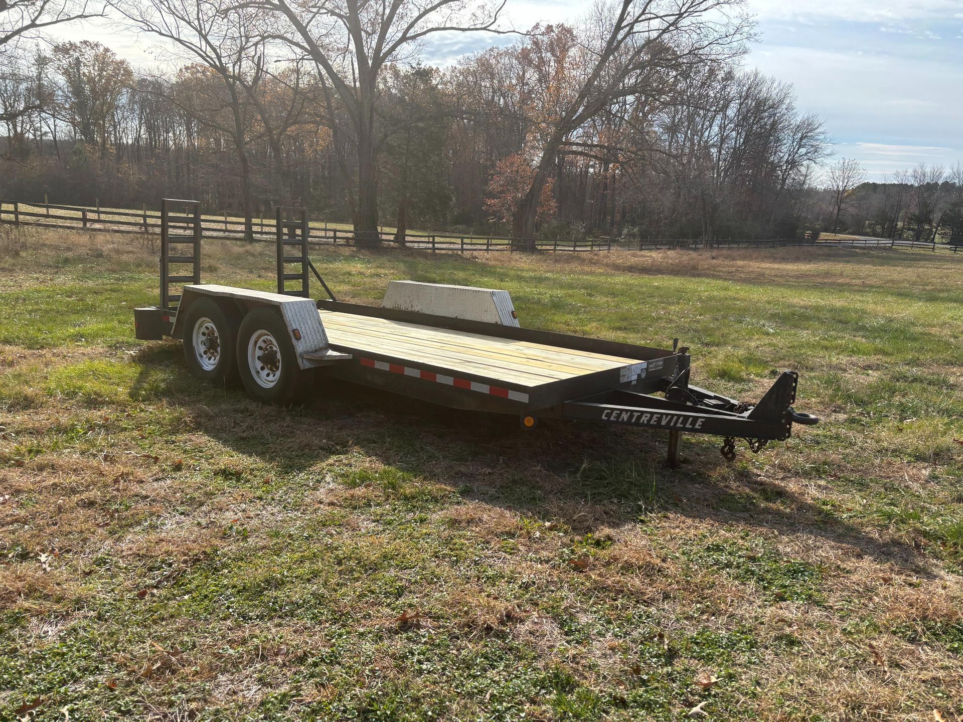 Black trailer on a grassy field with trees in the background.