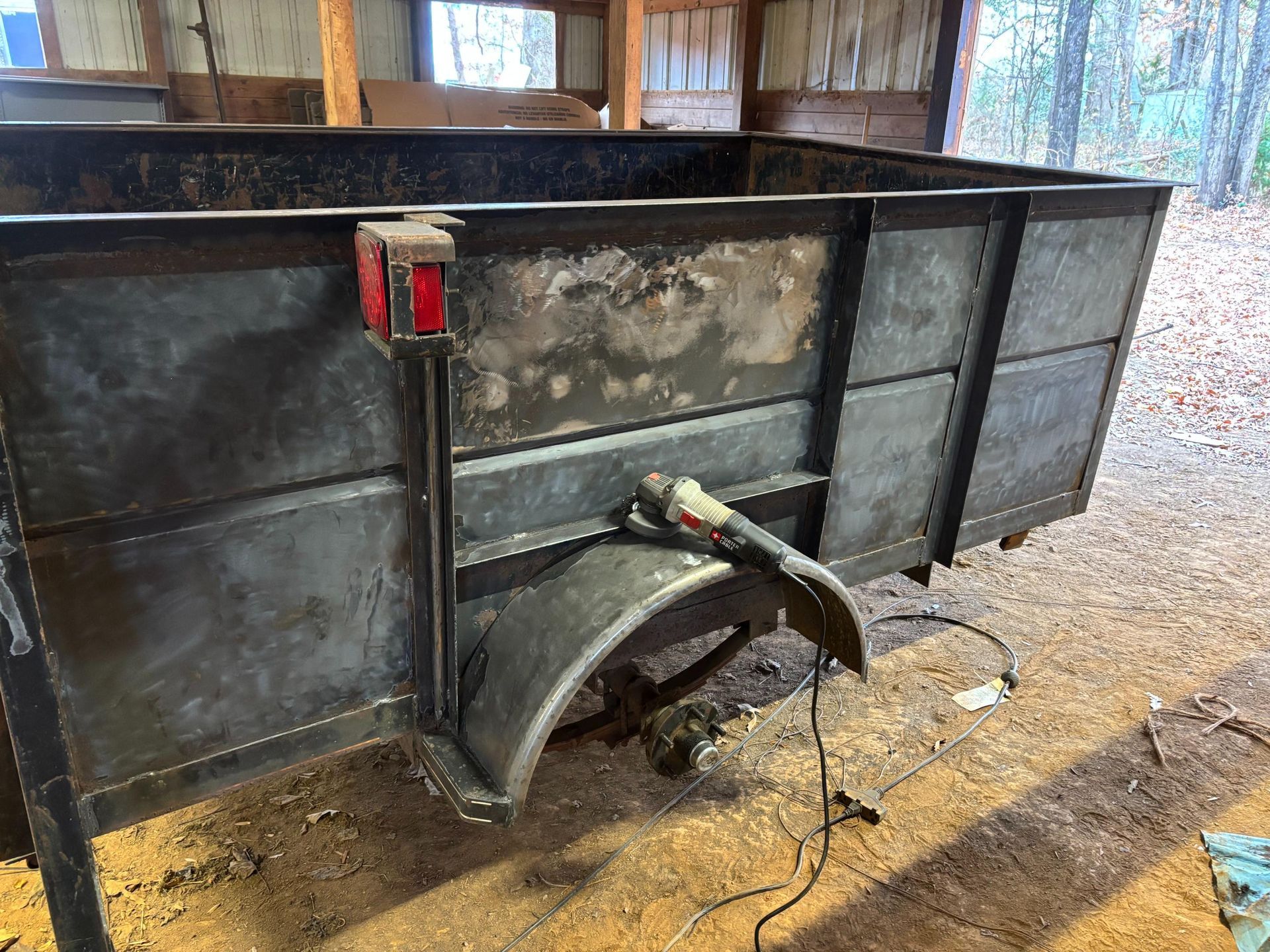 Metal trailer being worked on, grinder on fender. Dark metal, outdoor setting.