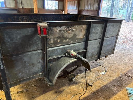 A metal utility trailer being worked on with a grinder; outdoors, daytime.