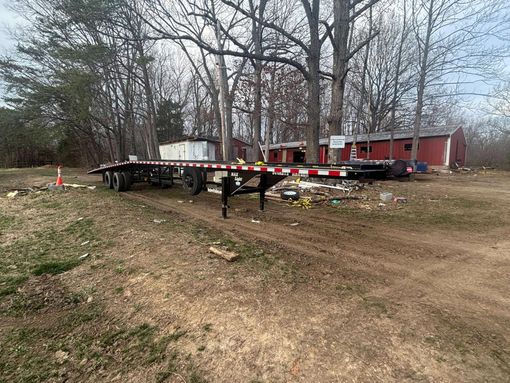 Black utility trailer in a yard with a white enclosed trailer in the background.