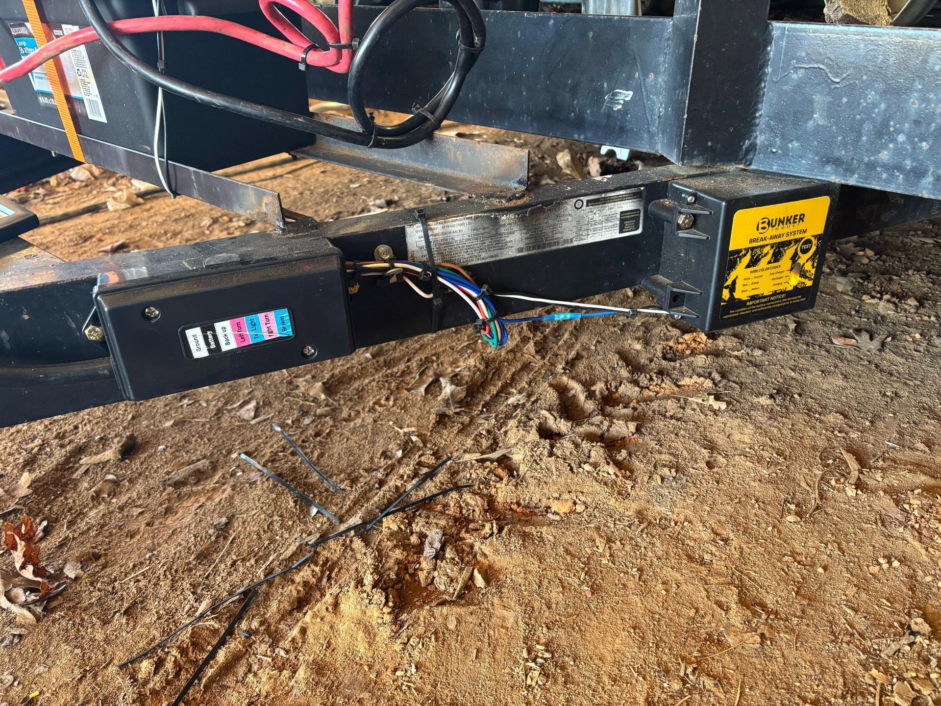 Exposed wiring on the tongue of a black metal trailer frame, with a battery box and yellow warning label visible.