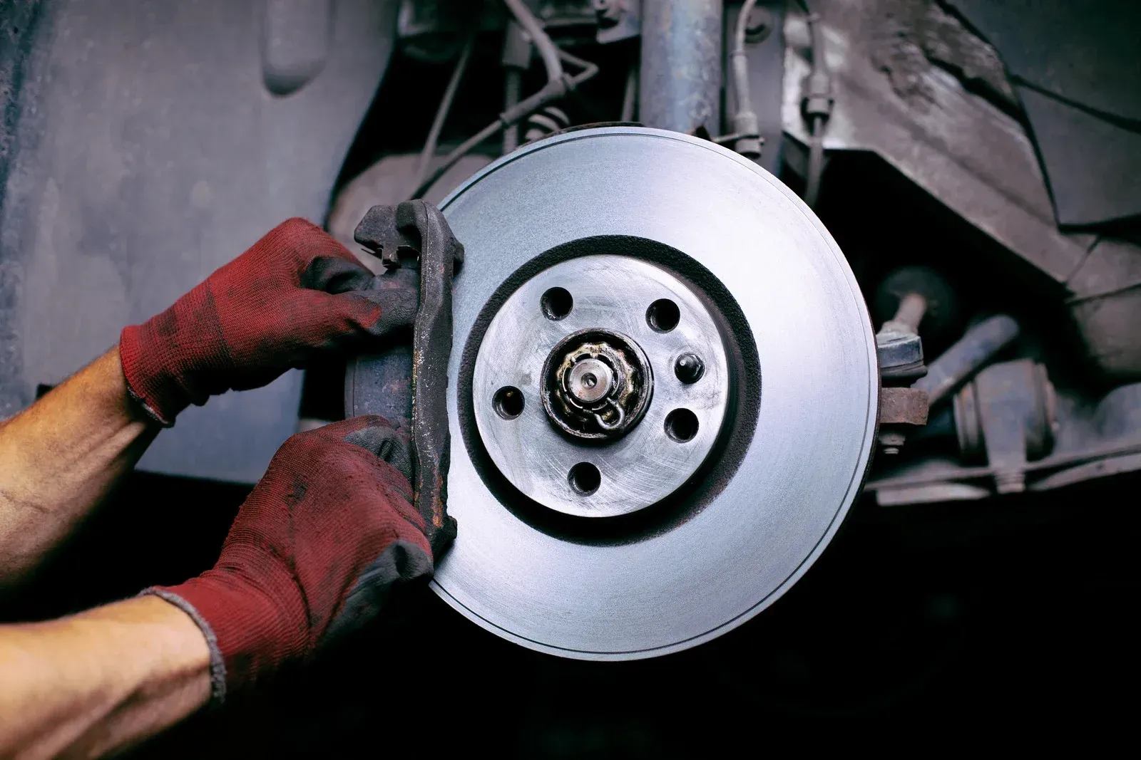 A person wearing red gloves is fixing a brake disc on a car.