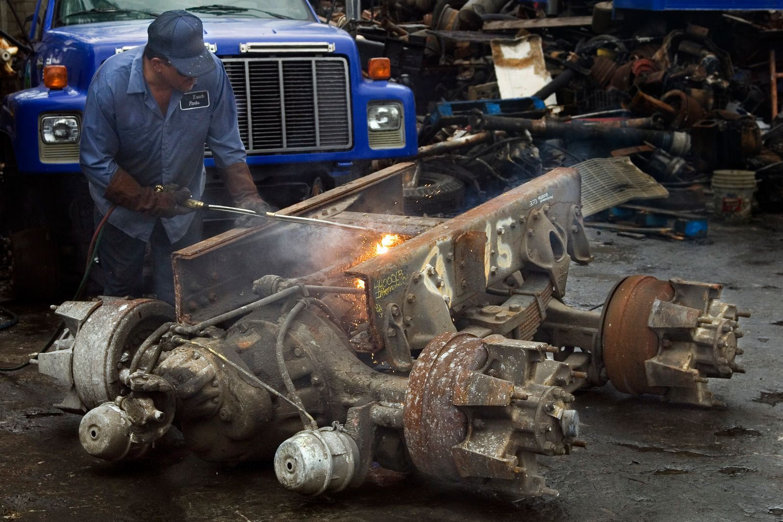 A man is cutting a piece of metal in front of a blue truck