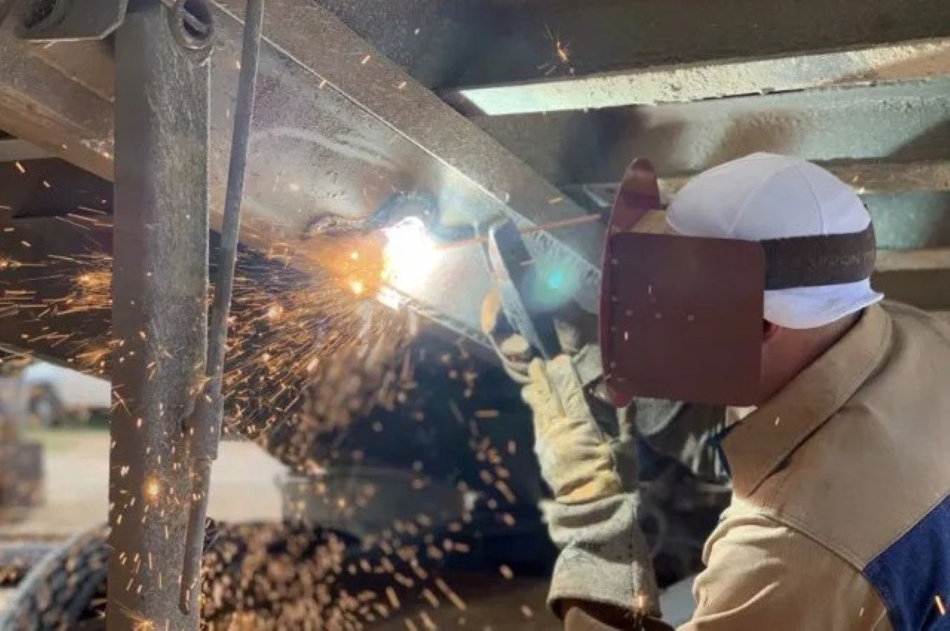 A man wearing a welding mask is welding a piece of metal.