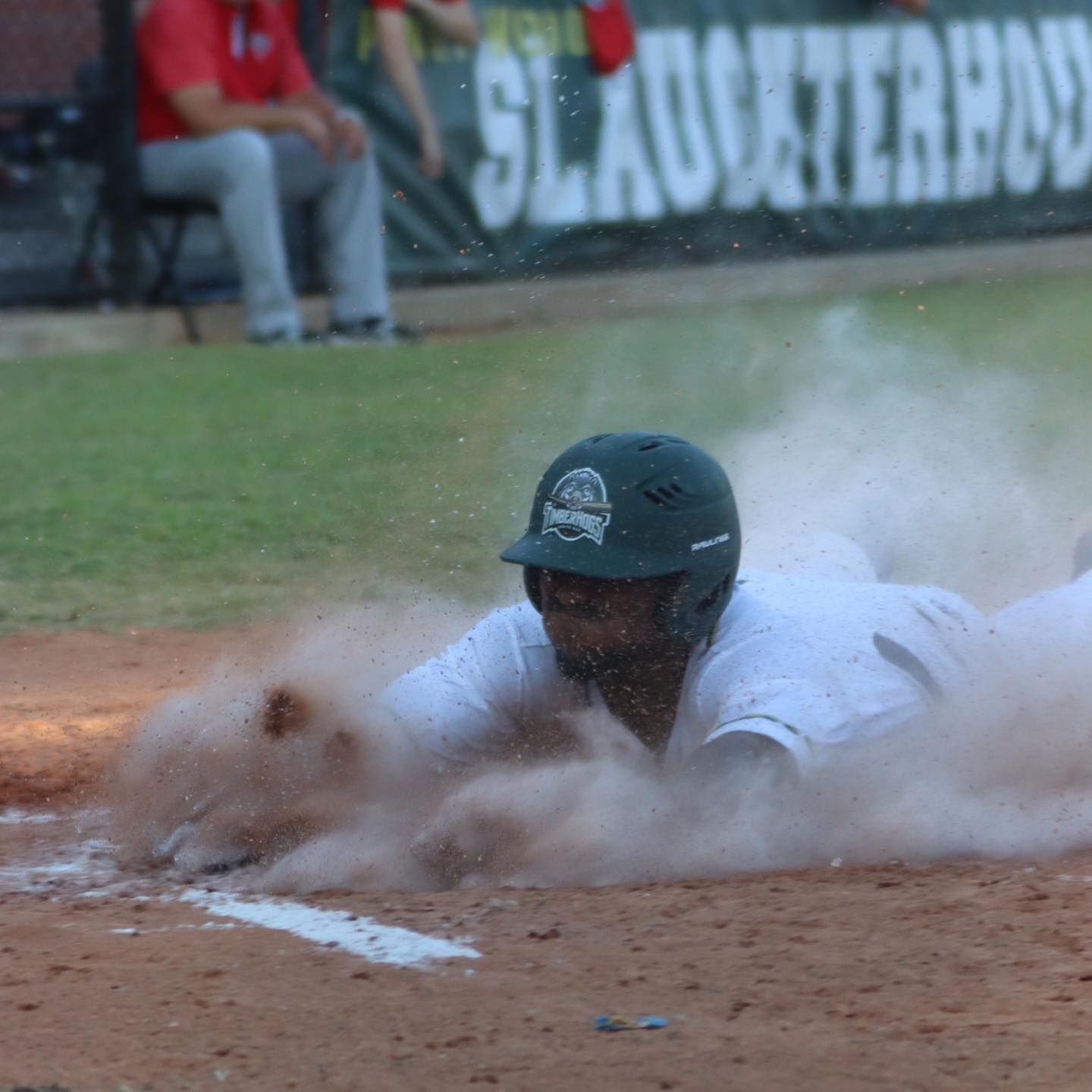 Baseball player sliding into home plate, kicking up dirt, wearing a green helmet and white uniform.