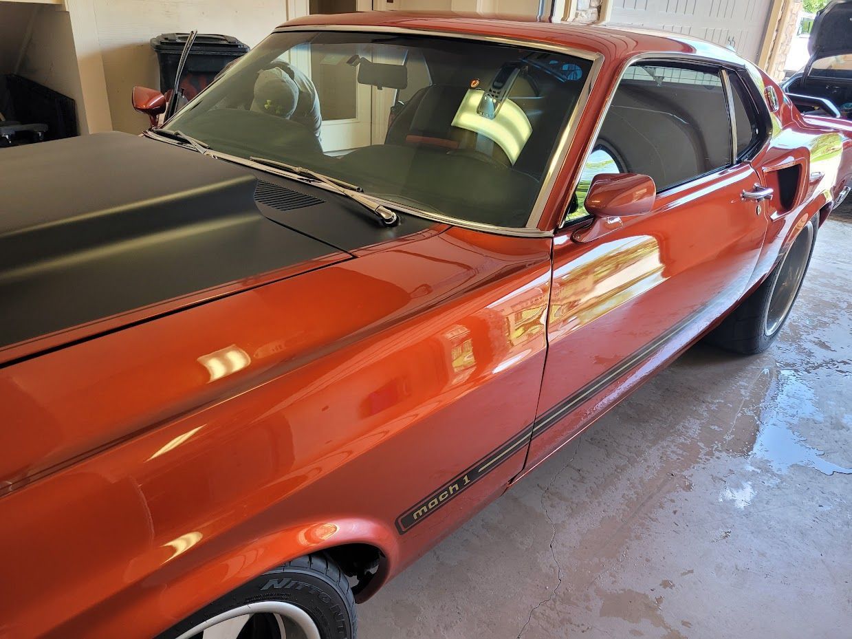 Orange 1969 Ford Mustang Mach 1 with black hood stripes, parked inside.