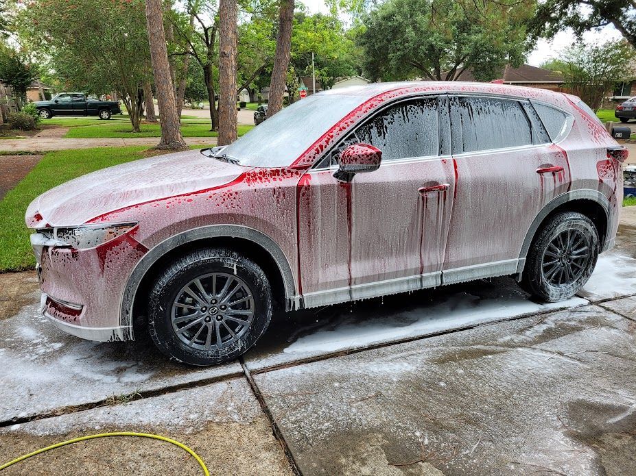 Red Mazda SUV covered in soap, parked on a driveway, being washed.