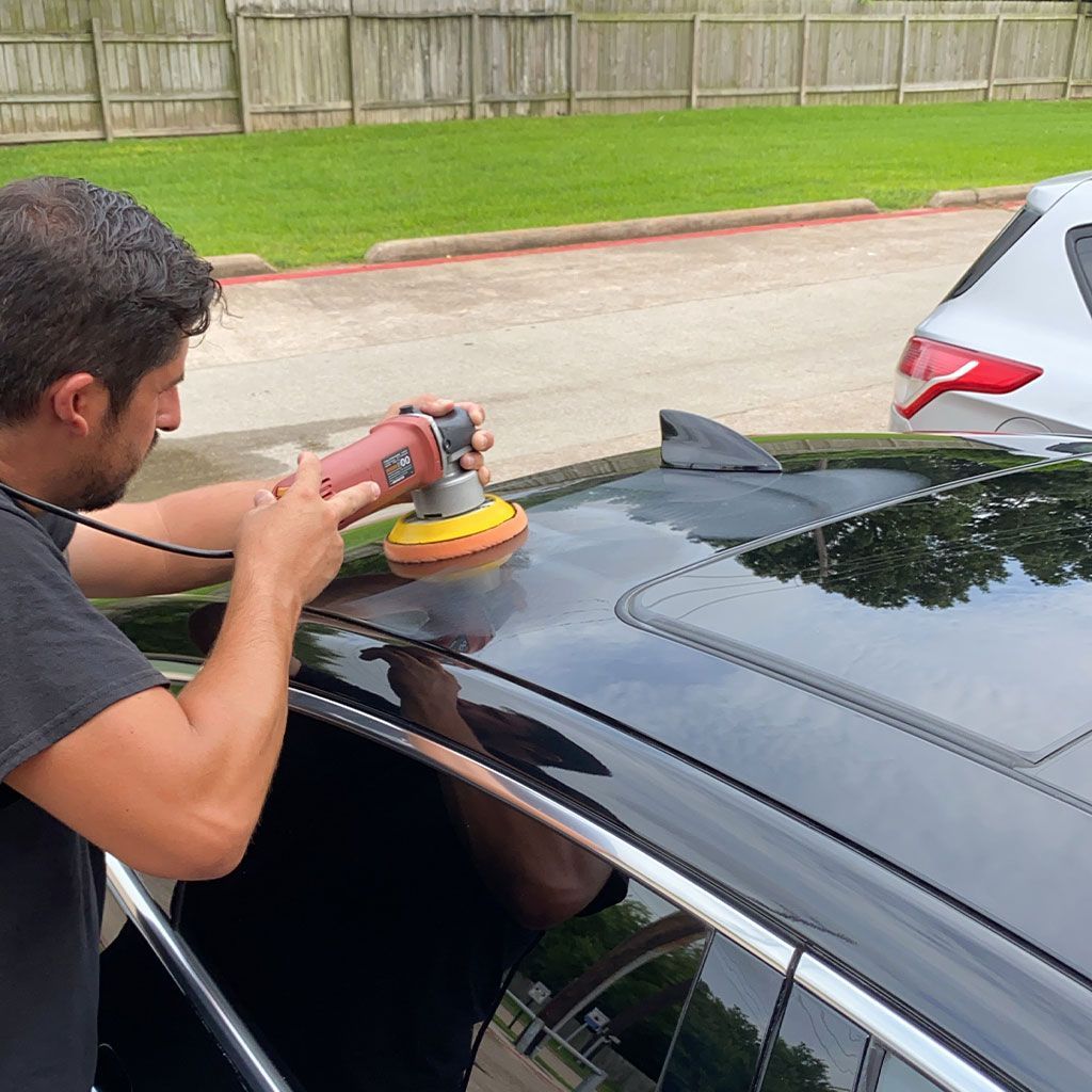 Man polishing a black car roof with a power buffer outdoors.