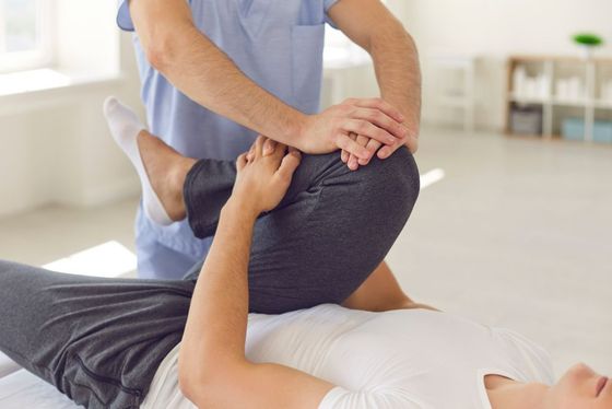 A man is stretching a woman 's leg on a bed.