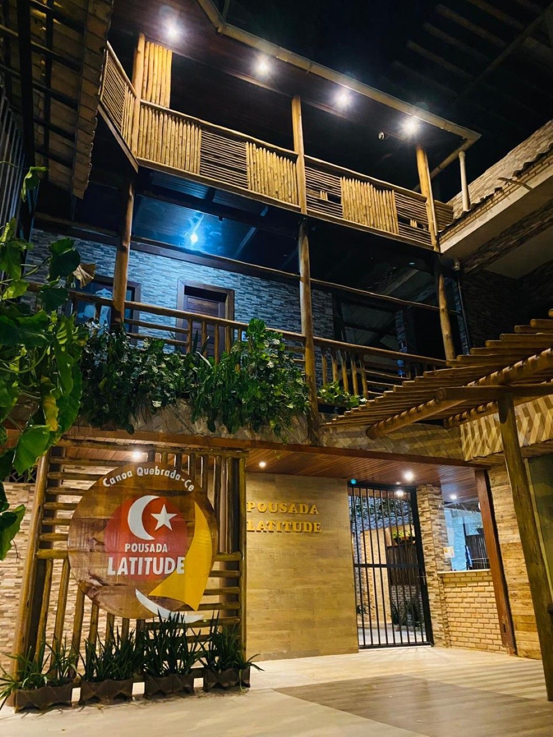 Fachada do hotel com detalhes em madeira, iluminada à noite. A placa diz "Posada Latitude".