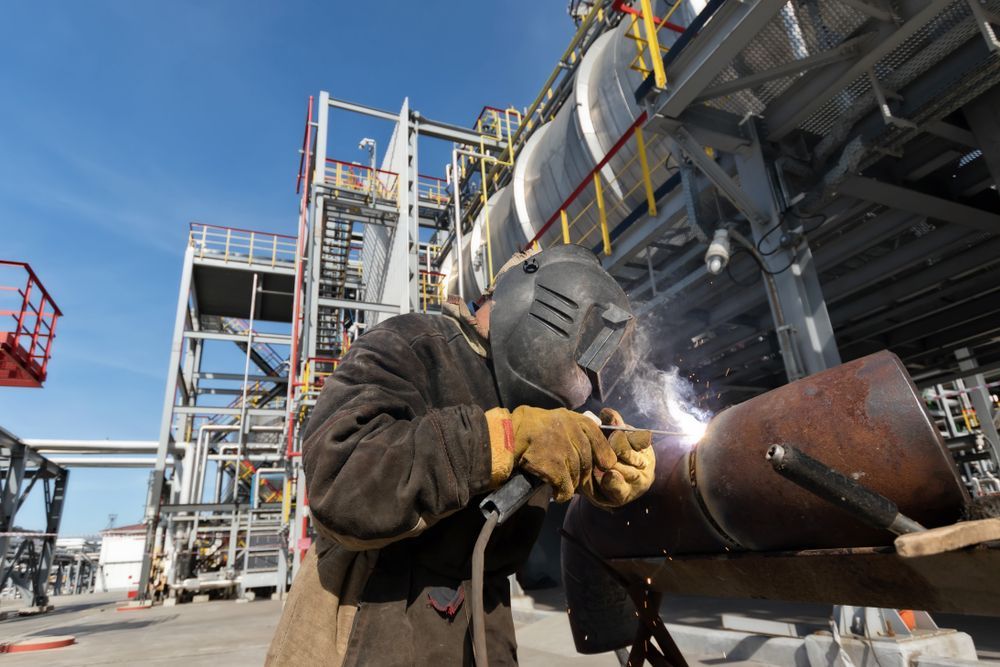 A Man Is Welding a Pipe in A Factory — Betts Welding Pty Ltd In Moss Vale, NSW