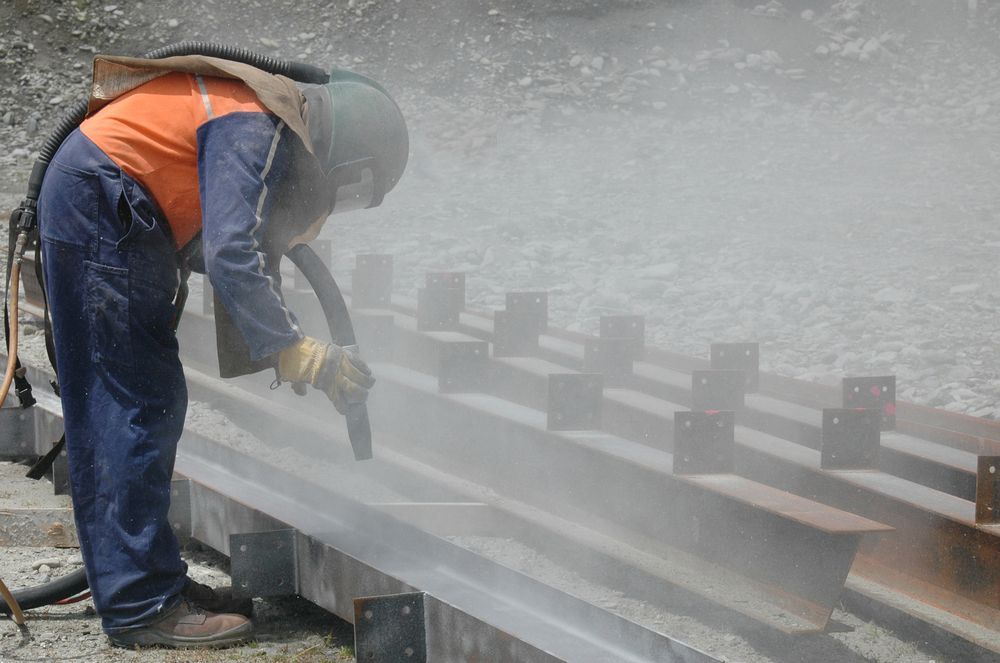 A man is sandblasting a piece of metal on a railroad track — Betts Welding Pty Ltd In Moss Vale, NSW