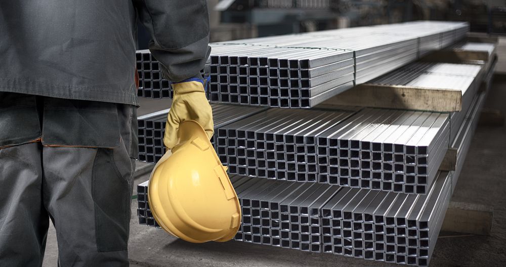 A Man Is Holding a Yellow Hard Hat in Front of A Stack of Metal Pipes — Betts Welding Pty Ltd In Moss Vale, NSW