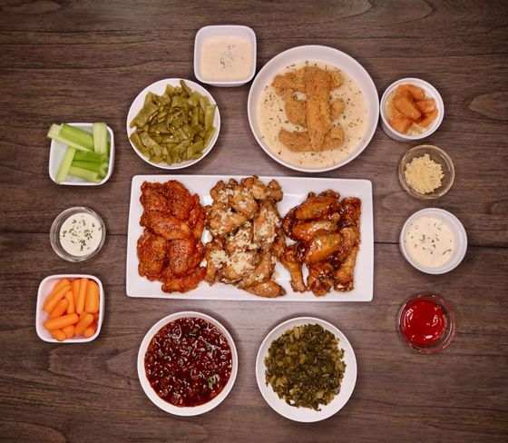 A table topped with plates of food including chicken wings and vegetables
