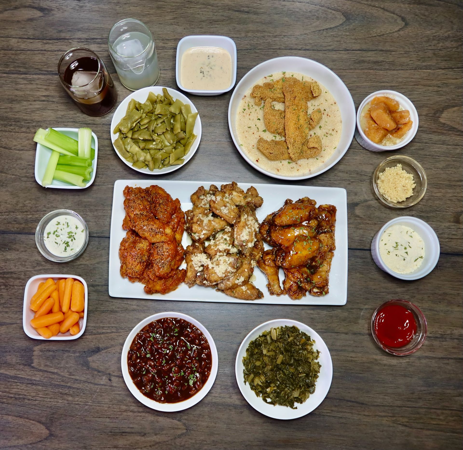 A wooden table topped with plates of food including chicken wings and vegetables.