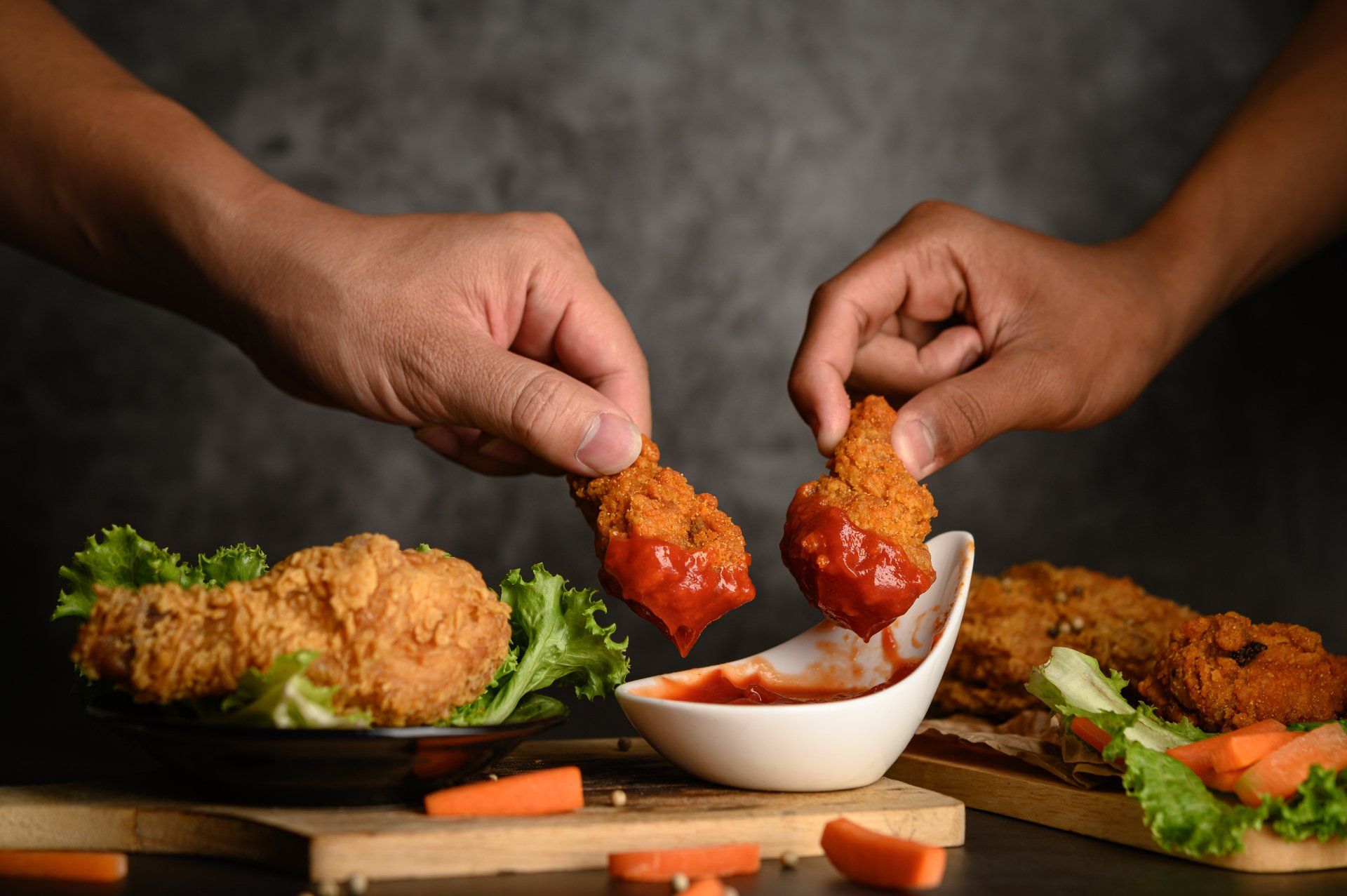 Two people are dipping fried chicken wings in sauce.