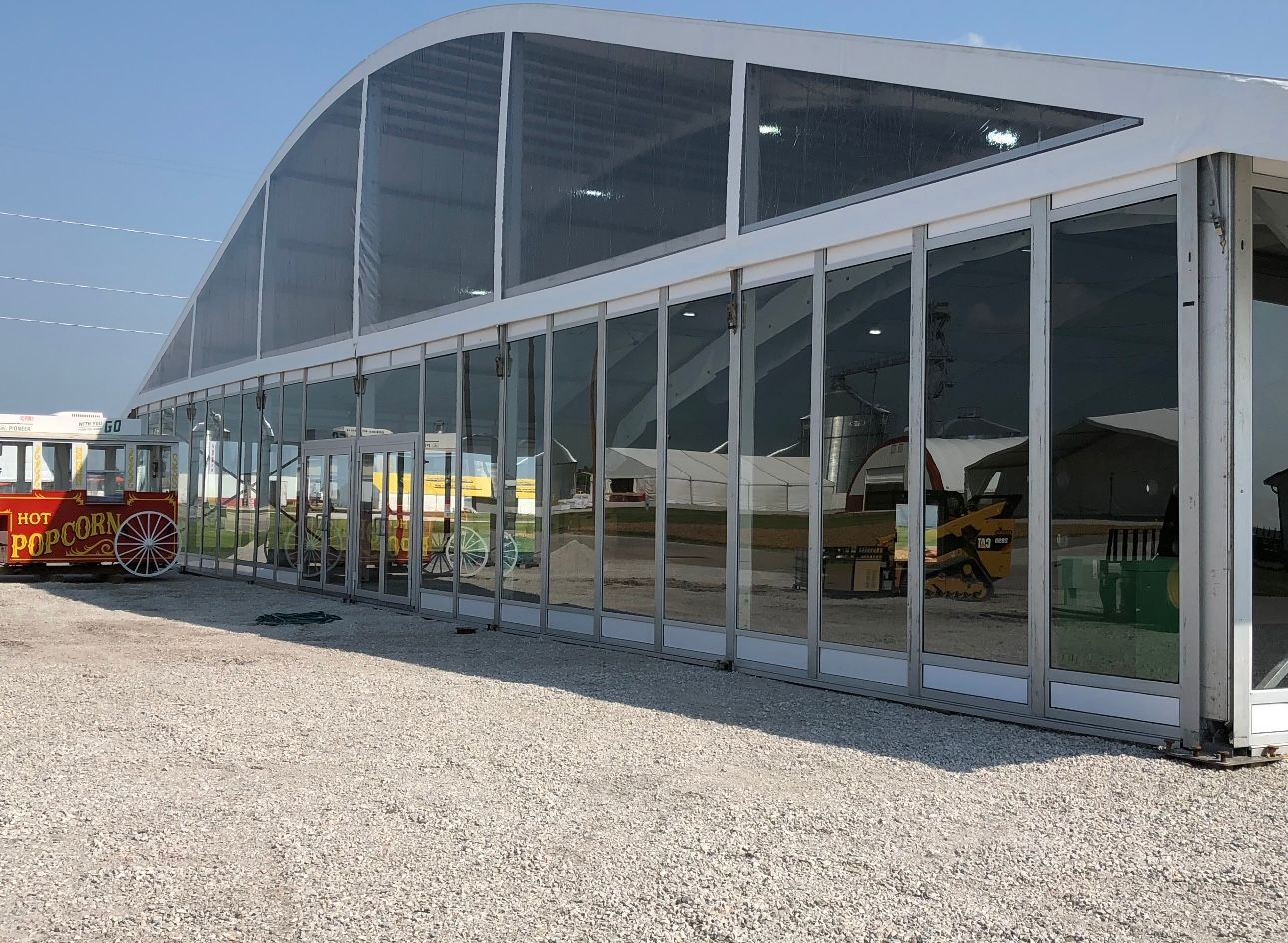 A large tent with a lot of windows is sitting in a gravel lot.