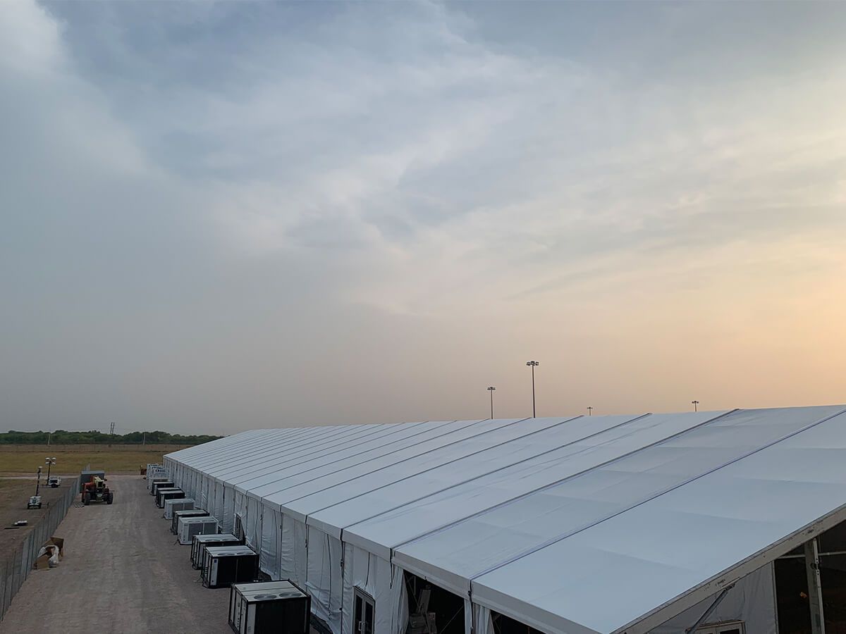 A row of white tents are lined up in a parking lot.