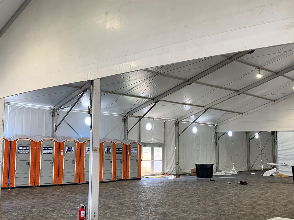 A large white tent with orange portable toilets inside of it.