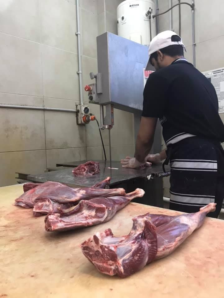 A Man Is Cutting Meat With A Band Saw In A Butcher Shop — Suhana Butcher & Grocery Shop In Millner, NT