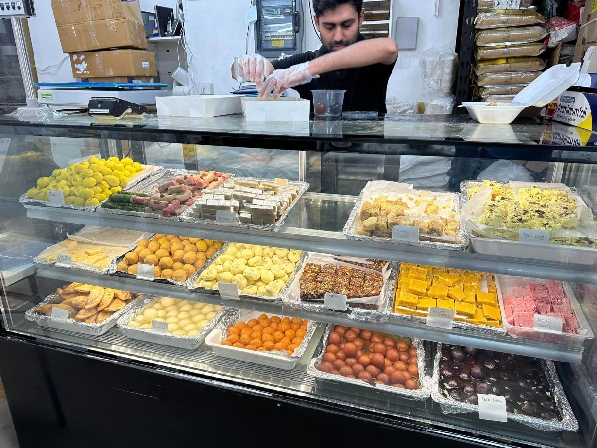A Man Is Standing Behind A Glass Display Case Filled With Lots Of Food — Suhana Butcher & Grocery Shop In Millner, NT