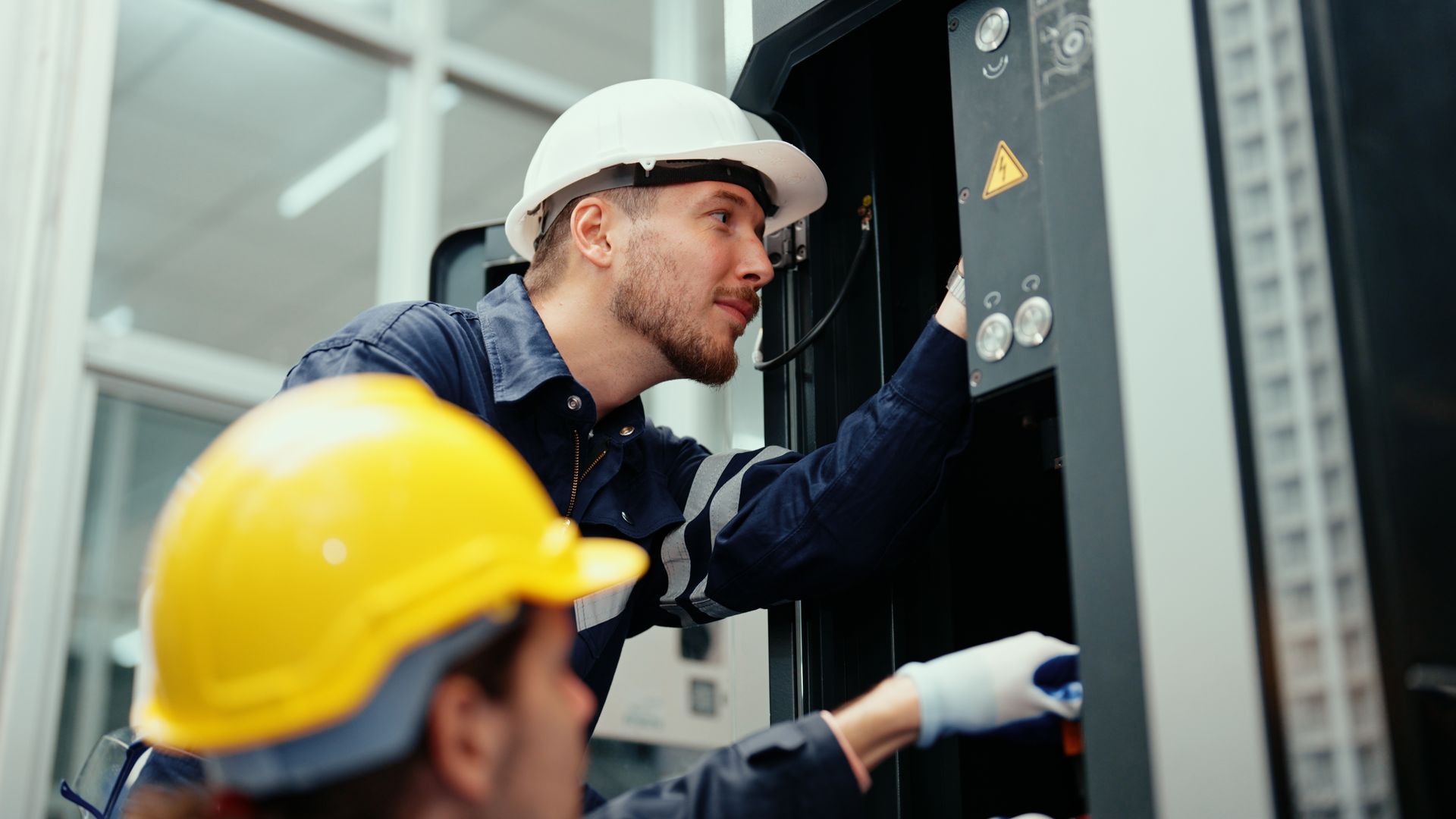 Two men in hard hats are working on a machine.