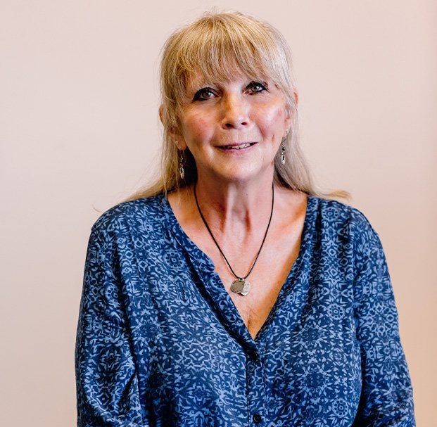 A woman wearing a blue shirt and a necklace is smiling for the camera.