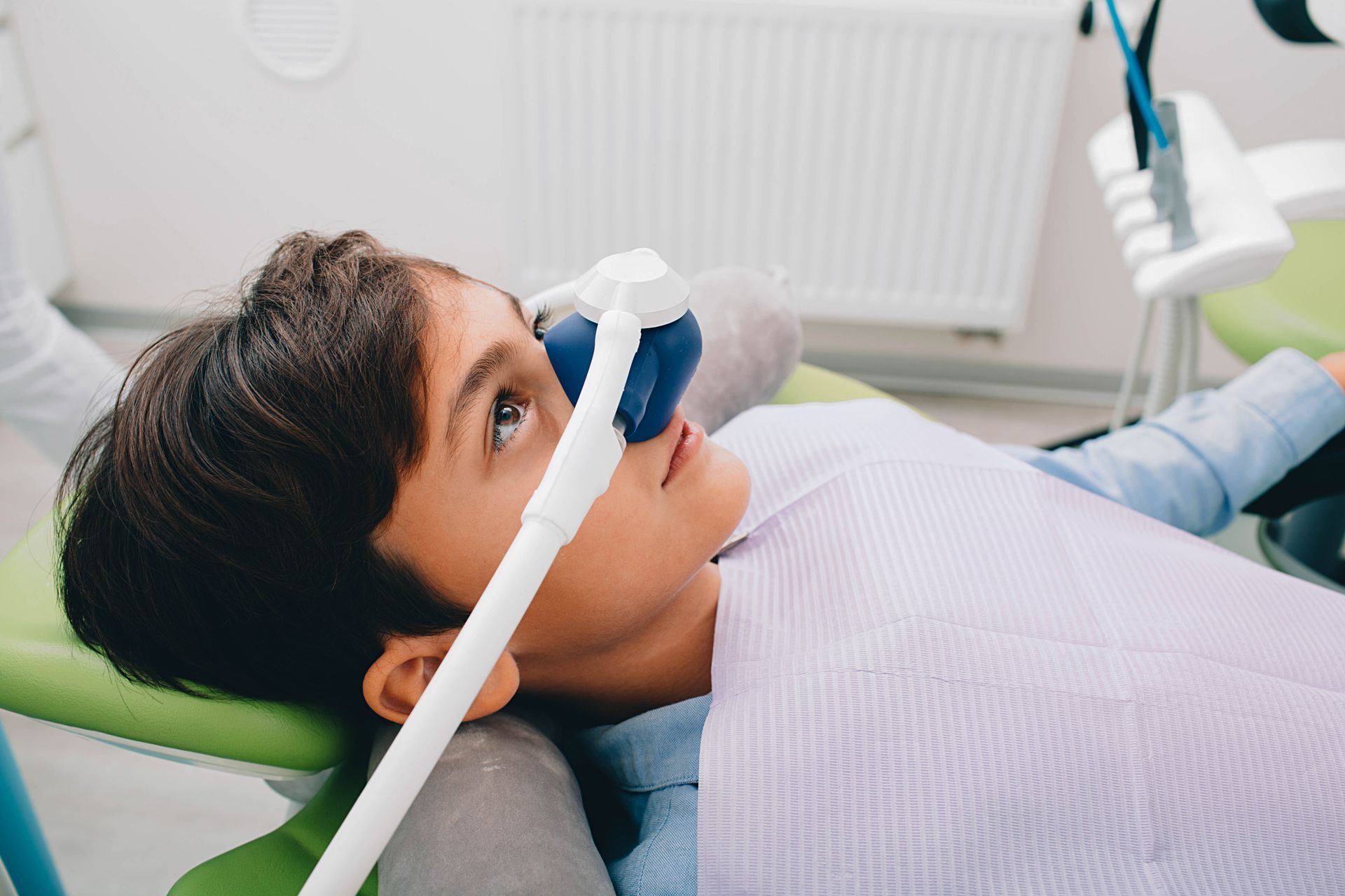 A young boy is laying in a dental chair with an oxygen mask on his face.