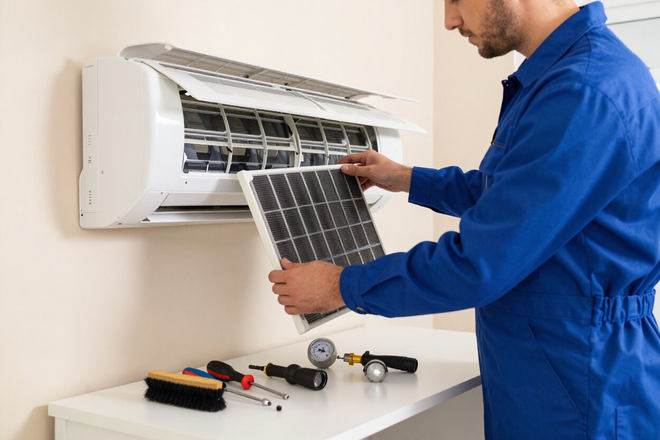 Technician cleaning a wall-mounted air conditioner with tools on a table below.